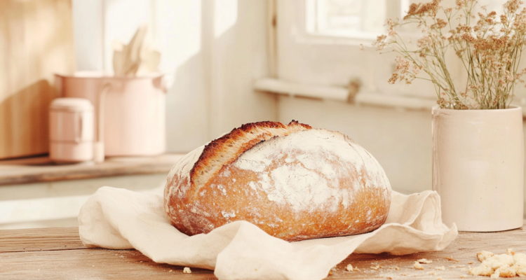 Cinematic shot of a freshly baked loaf of bread placed on a rustic wooden kitchen counter. The bread is golden brown with a crisp crust and soft, fluffy texture, surrounded by scattered crumbs.